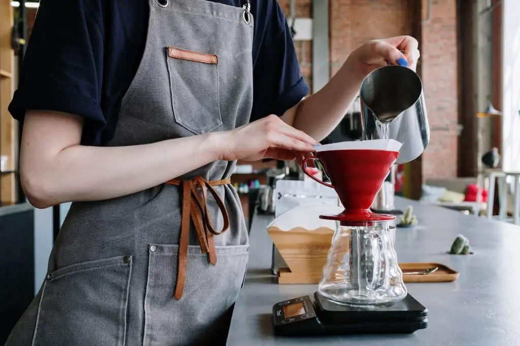 person in gray apron holding red ceramic bowl